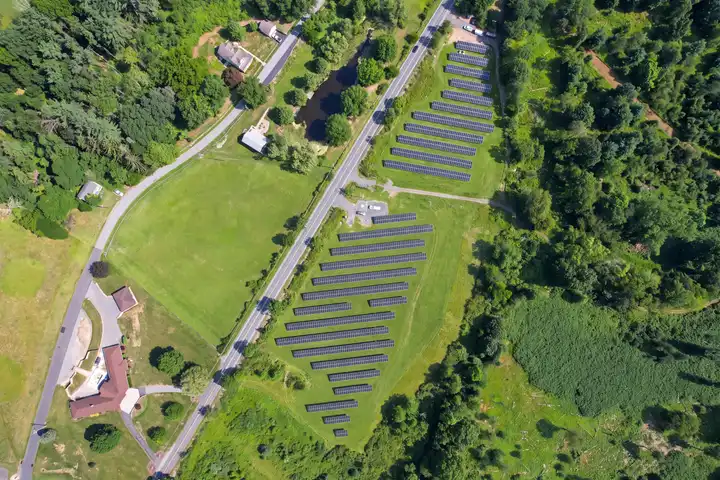 The Adamsdale solar array in Schuylkill Haven, PA, seen from directly above: two blocks of solar panel rows on cleared land beside a two-lane road, with woods and fields around
