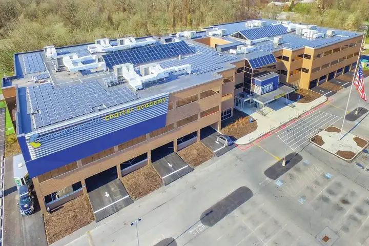 Commonwealth Charter Academy in Harrisburg, PA, from above, with rows of solar panels across its roofs and the school's sign at the entrance.