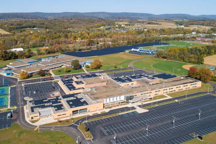 A drone view over Central Columbia's high school and middle school campus in autumn, with solar panels on several roofs and a long array in the field behind