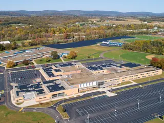A drone view over Central Columbia's high school and middle school campus in autumn, with solar panels on several roofs and a long array in the field behind