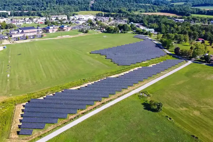 A ground-mounted solar array beside a school's playing fields, seen from a drone