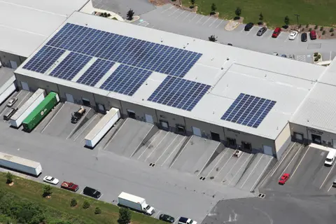 Aerial view of three blocks of solar panels on the warehouse's metal roof, with its loading docks and parking lots