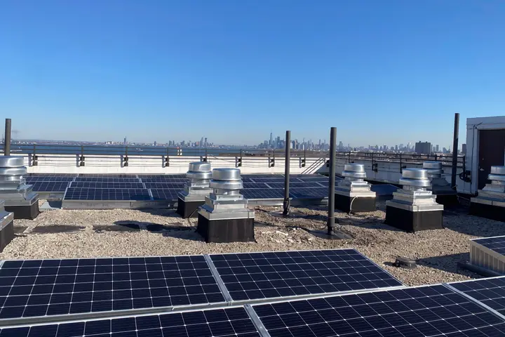 Rows of solar panels on the roof of Shore Hill Apartments in Brooklyn, NY, with the Manhattan skyline beyond