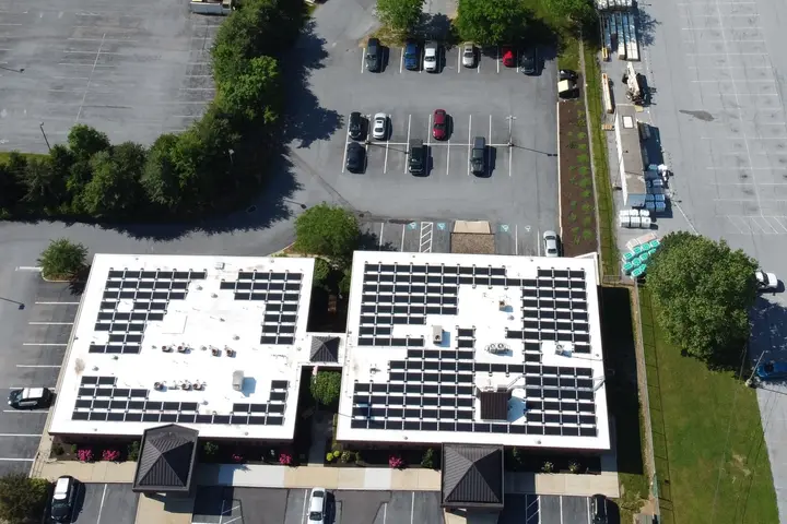 Rows of solar panels across the white roofs of Susquehanna Township buildings in Harrisburg, PA, seen from above, with the parking lots around them
