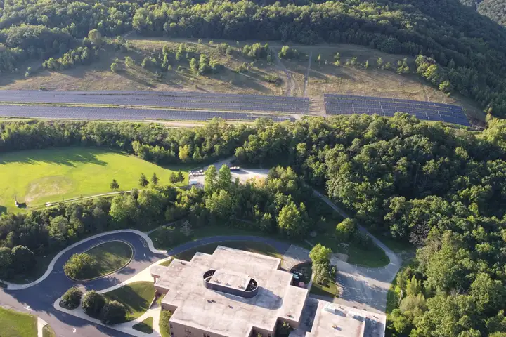 Aerial view of two long ground-mounted solar arrays on a hillside above Tamaqua Elementary, its sports field and wooded hills